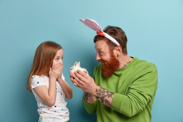 Happy father gives small fluffy rabbit to his daughter, makes present