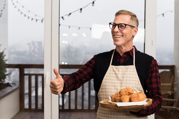 Happy father giving thumbs up while holding plate of muffins