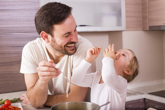 幸せな父と彼の小さな娘がキッチンで自家製スパゲッティを食べています