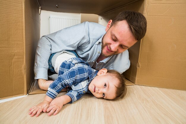 Счастливый отец, играя со своим сыном малыша в движущейся картонной коробке