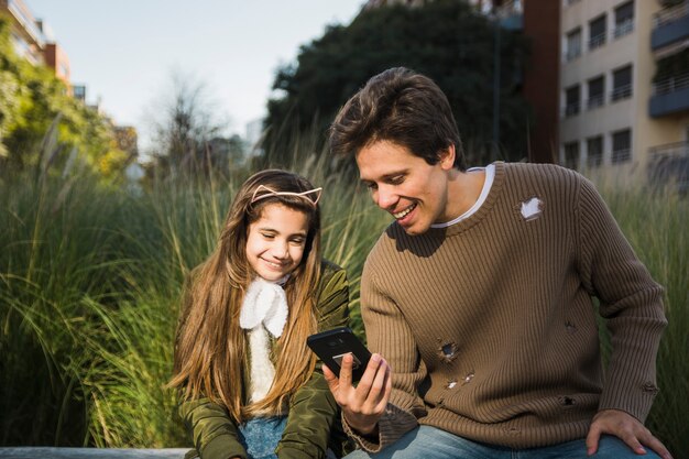Счастливый отец показывает что-то своей дочери на мобильном телефоне