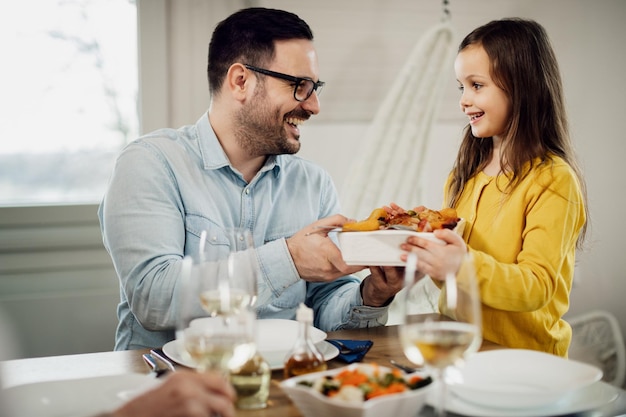 彼女が食堂で昼食時に彼に食べ物を提供している間、彼の小さな娘と話している幸せな父