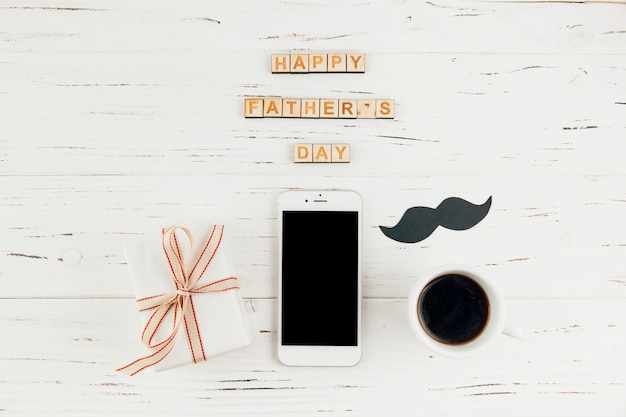 Happy fathers day words near smartphone with gift and cup of drink