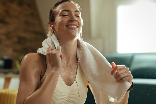 休憩しながらイヤホンで音楽を聴きながら汗を拭く幸せな女性アスリート。