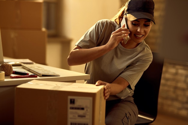 オフィスで荷物をチェックしながら電話で話している幸せな女性の宅配便