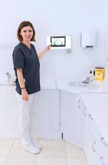 Happy female dentist pointing at teeth x-ray in clinic