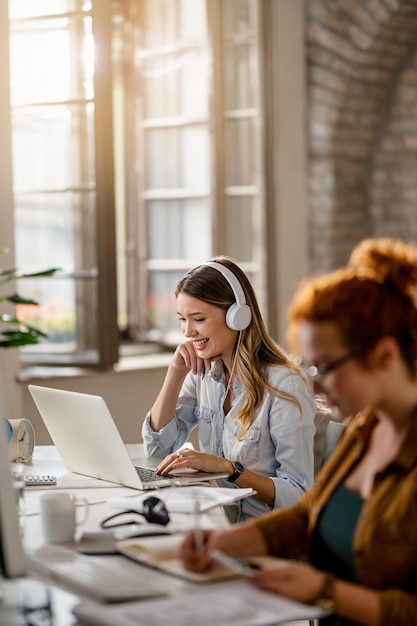 Happy female freelancer working on a computer while listening
music over headphones in the office