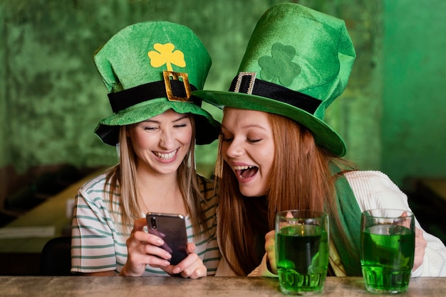 Happy female friends celebrating st. patrick's day together at the bar with smartphone