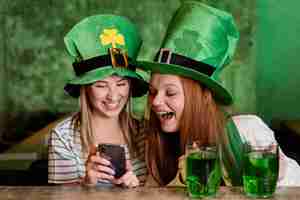 Foto gratuita amici femminili felici che celebrano st. patrick's day insieme al bar con lo smartphone