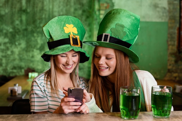 Foto gratuita amici femminili felici che celebrano st. patrick's day insieme allo smartphone al bar