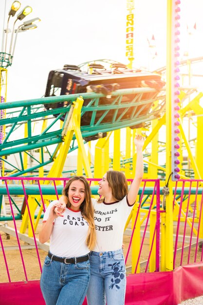 Happy female friends hanging out together in front of roller coaster ride