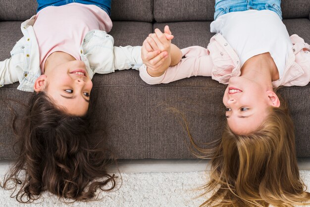 Happy female friends lying on sofa with her head upside down