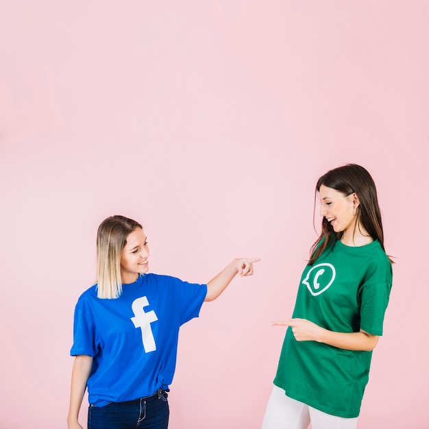 Happy female friends pointing at each other on pink background