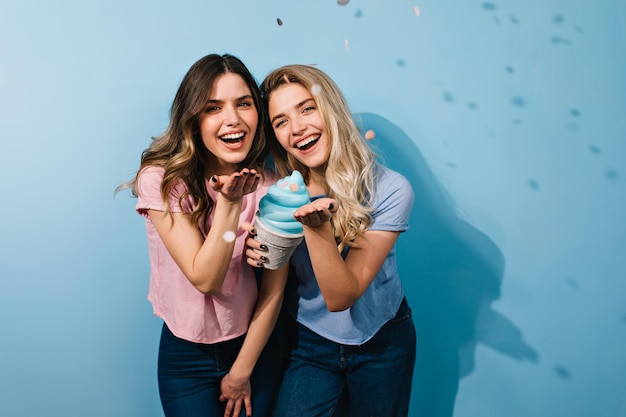 Happy female friends posing under confetti Studio shot of stunning girls with toy ice cream