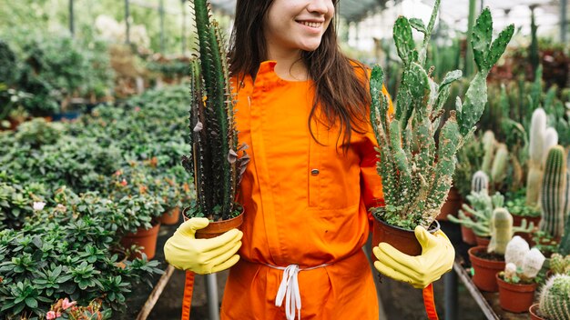 サボテンを保持している幸せな女性の庭師は、温室で植物を鉢植えにした
