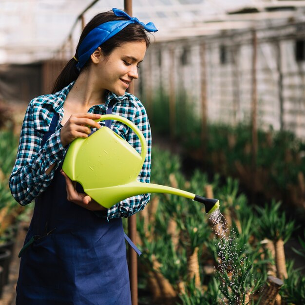 Happy female gardener watering plants in greenhouse