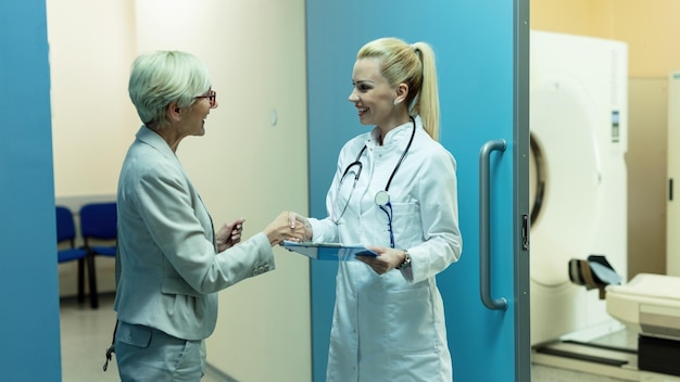 Happy female general practitioner and her mature patient greeting and shaking hands ta clinic