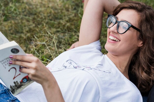 Happy female lying on grass reading book
