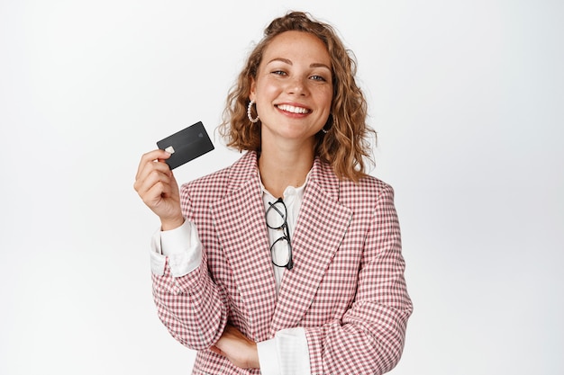幸せな女性マネージャーは、クレジットカードと笑顔を見せて、白地にスーツを着て立っています