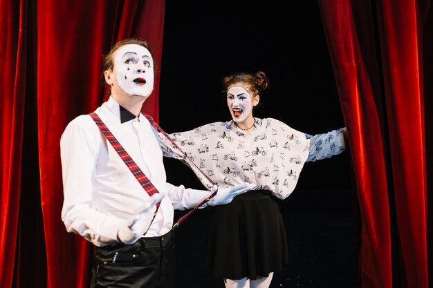 Happy female mime looking at male mime holding suspender on stage