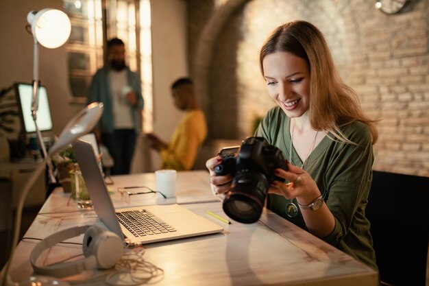 Счастливая женщина-фотограф проверяет изображения на цифровой камере, работая ночью в студии