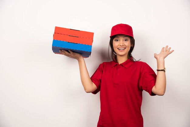 Счастливый женский работник доставки пиццы стоя с тремя картонами пиццы.
