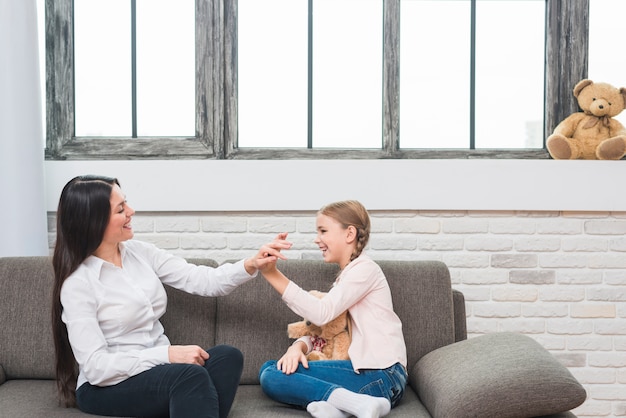 Happy female psychologist giving high five to little girl sitting on sofa at home