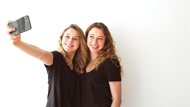 Happy female sister taking self portrait on mobile phone against white backdrop