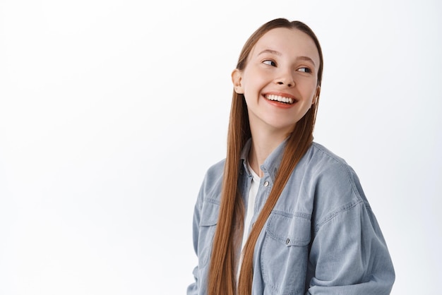 행복한 여학생 10대 소녀가 어깨 뒤를 바라보고 로고 회사 배너 흰색 배경에 대해 copyspace 근처에 평온한 미소를 짓고 있습니다.