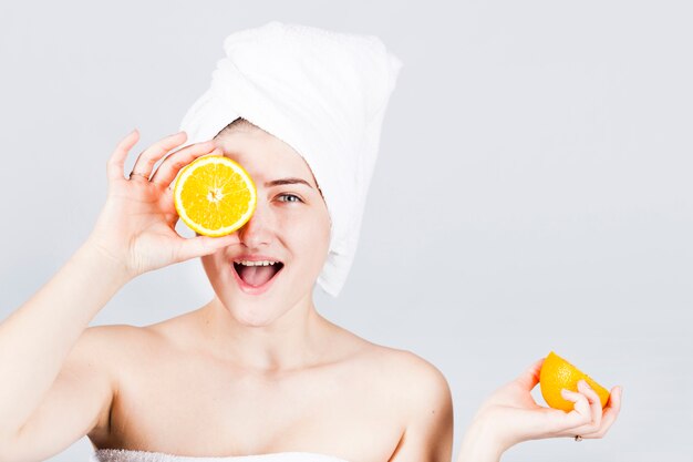 Счастливый женщина в полотенце с апельсинами на лице