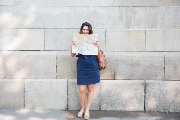 Happy female traveler consulting map in street