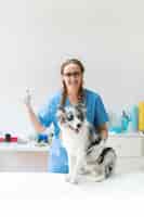 무료 사진 엄지 손가락 기호를 보여주는 테이블에 강아지와 함께 행복 한 여성 수의사