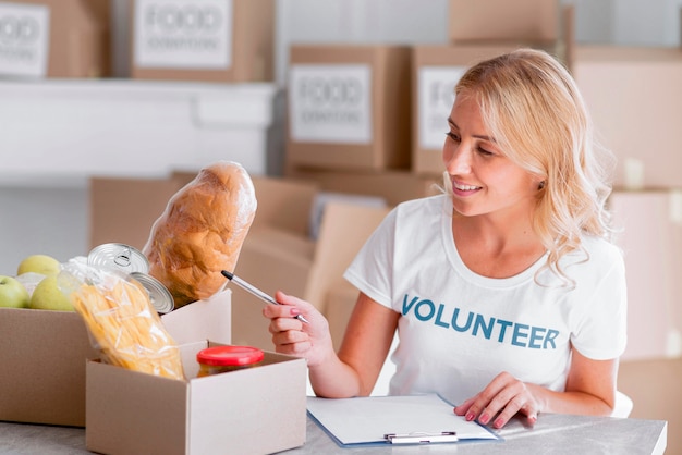 Free Photo happy female volunteer putting food in boxes for donation