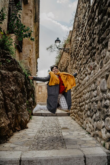Счастливая женщина в теплой одежде прыгает в переулке