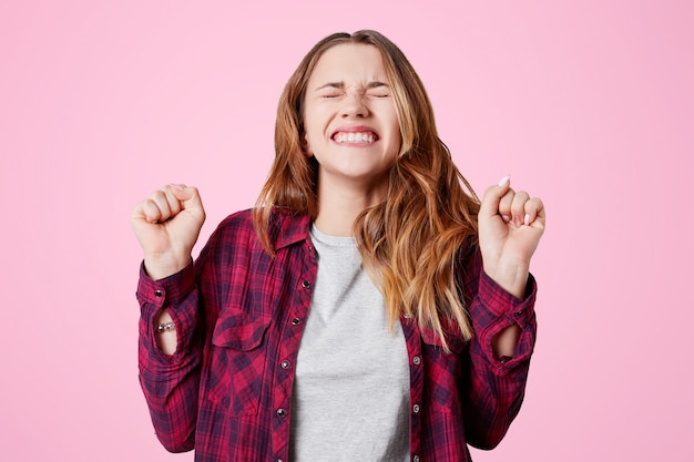 Foto gratuita felice donna vincitrice con un piacevole sorriso, stringe pugni e denti, si rallegra della sua vittoria o del suo grande successo