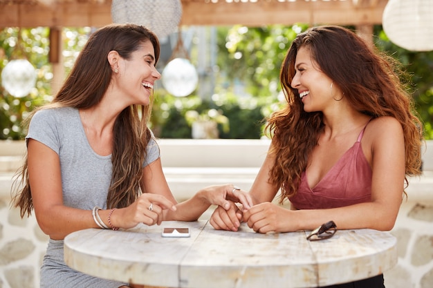 Happy females with dark luxurious hair, have meeting together at cozy coffee shop, enjoy calm atmosphere and intimacy