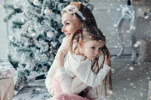 Happy festive mother and daughter hugging sitting together at decorating beautiful christmas tree