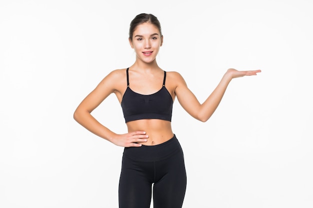 Happy fitness woman pointing finger at copyspace on her palm on a white wall