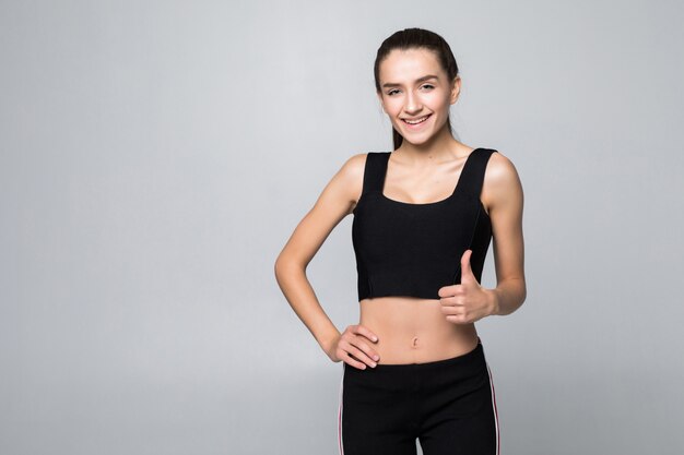 Happy fitness woman showing thumb up isolated on a white wall