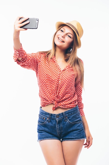 白い背景の上に、携帯電話で自分の写真を撮る幸せないちゃつく若い女性