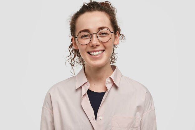 Happy freckled teenager with glasses posing against the white wall