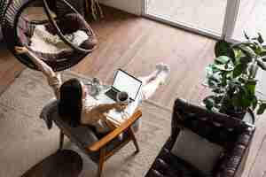 Free photo happy free asian girl sitting at home with laptop and coffee mug raising hands up