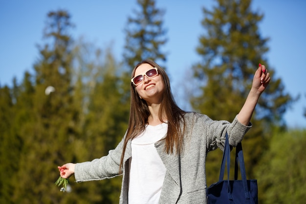 Foto gratuita felice donna libera nel parco in occhiali da sole, sorridente con le mani alzate.