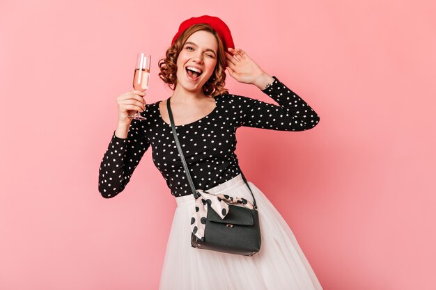 와인 글라스를 들고 행복 한 프랑스 소녀입니다. 분홍색 배경에 고립 된 베 레 모에 웃는 곱슬 여자의 스튜디오 샷.