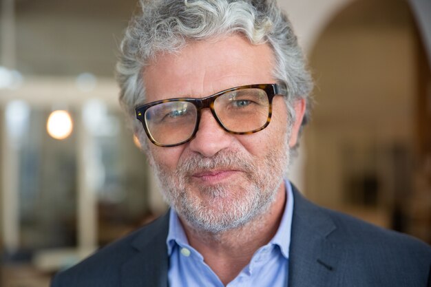 Happy friendly mature business man wearing jacket and glasses, posing indoors, looking at camera