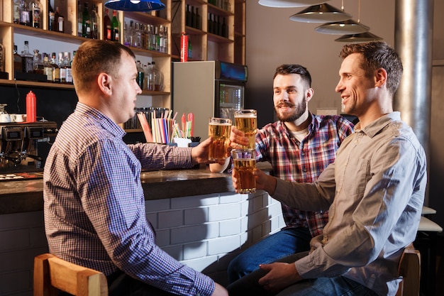 Happy friends drinking beer at counter in pub