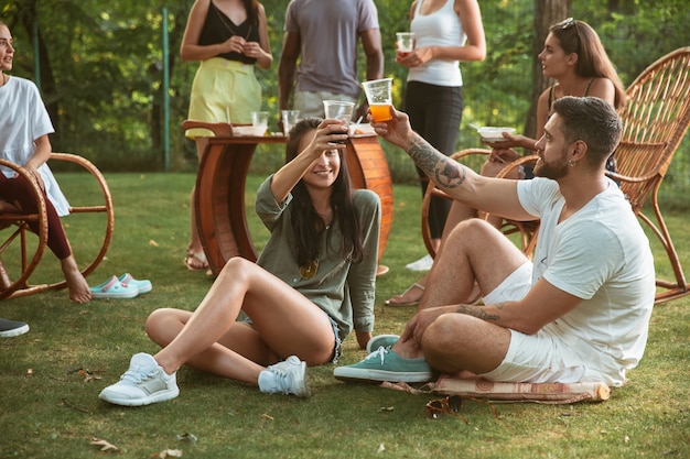 Foto gratuita amici felici che mangiano e bevono birre alla cena barbecue sull'ora del tramonto