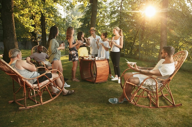 Foto gratuita amici felici che mangiano e bevono birre alla cena barbecue sull'ora del tramonto