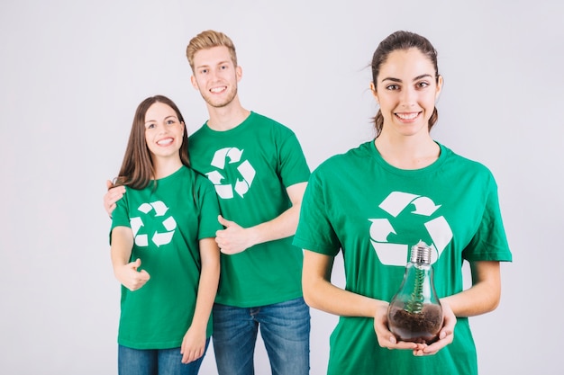 Happy friends gesturing thumbs up behind young woman holding sapling in light bulb