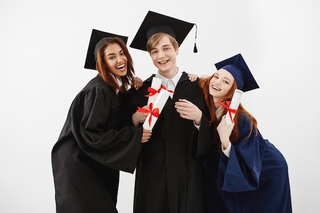 Happy friends graduates smiling holding diplomas.